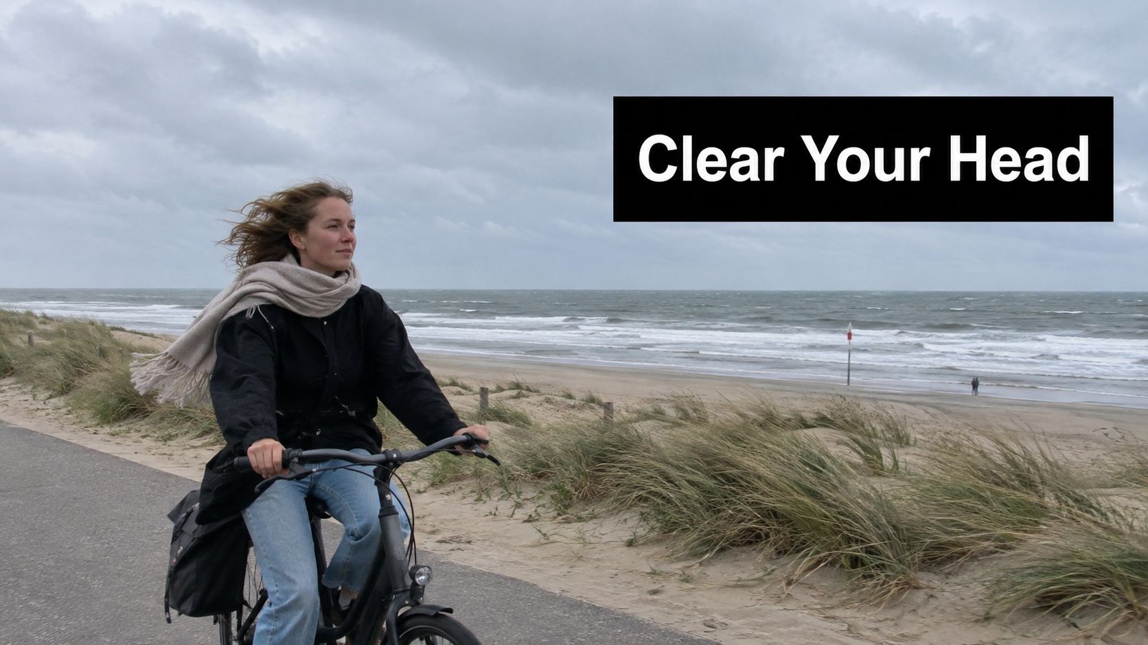 A young woman riding a bicycle along a sandy beach path on a cloudy day